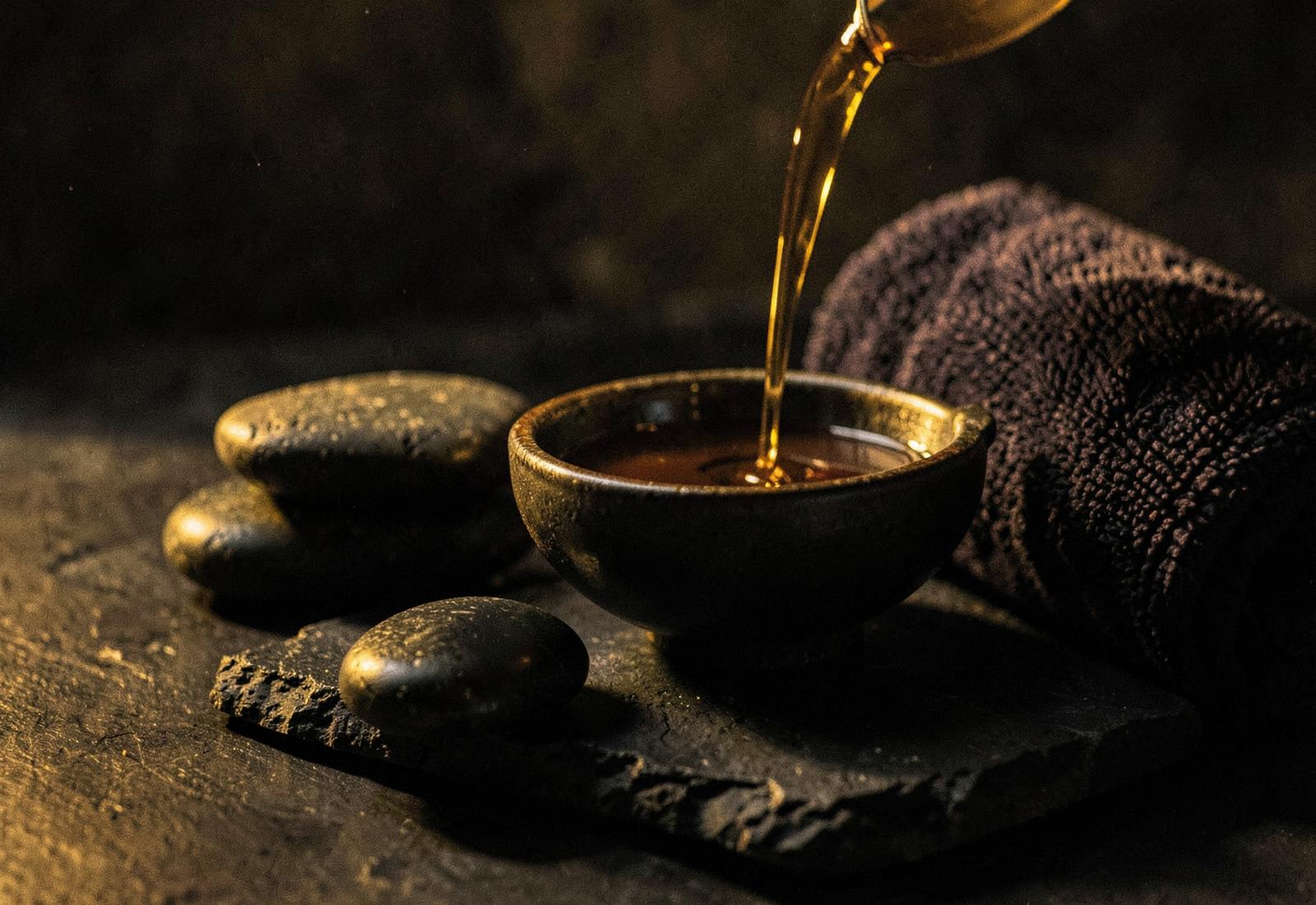 Warm treatment oil poured over massage stones in low golden light